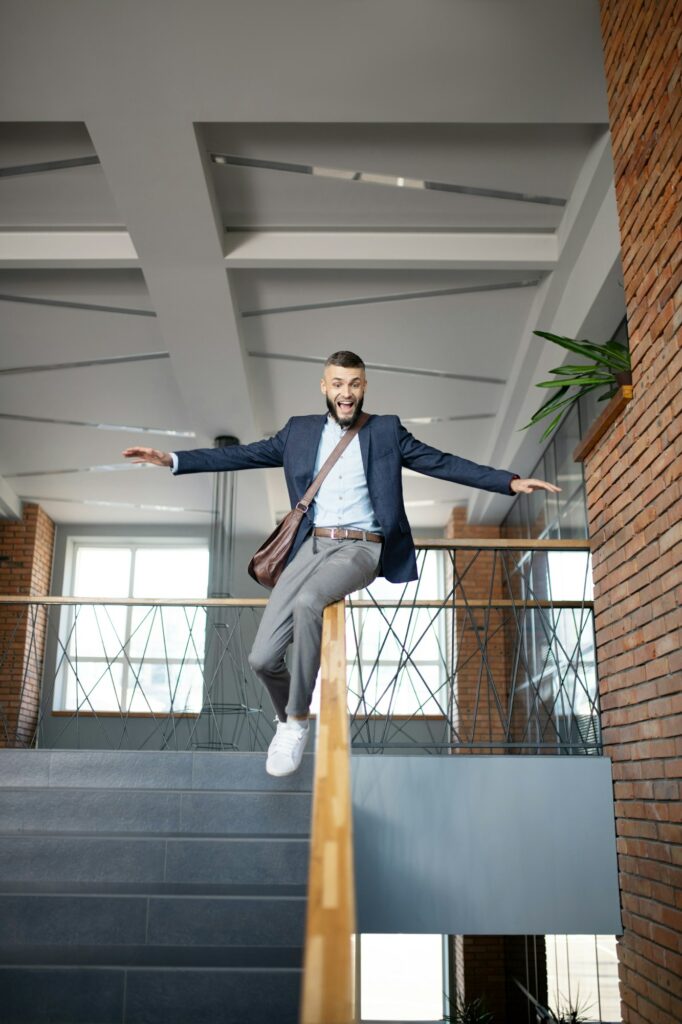 Happy office worker sliding on banister after finishing work